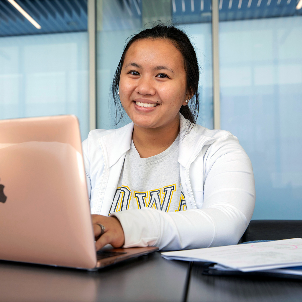 A female student working on her laptop smiling at the camera.